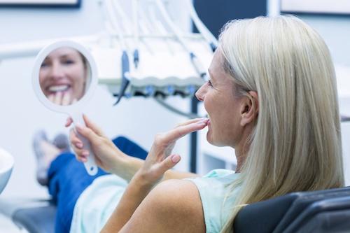 Older woman looking at teeth in mirror, indianapolis in